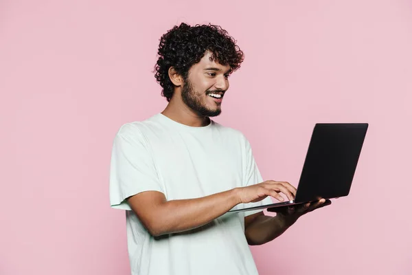 年轻的中东男子面带微笑 一边摆姿势 一边把笔记本电脑隔在粉红的墙上 — 图库照片