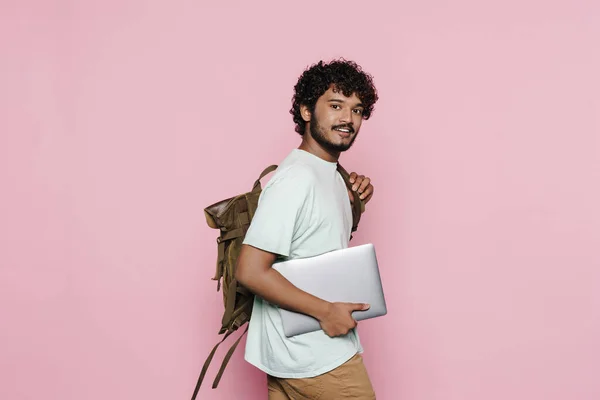 年轻的中东男子面带微笑 一边摆姿势 一边拿着手提电脑和背包 隔着粉红的墙壁 — 图库照片