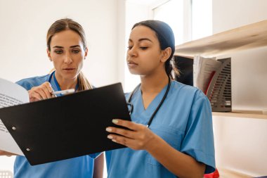 Ofiste evraklarla çalışırken çok ırklı kadın doktorlar konuşuyor.