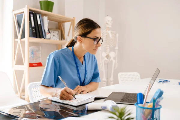 White Woman Doctor Writing Notes While Working Laptop Office Indoors — Foto Stock