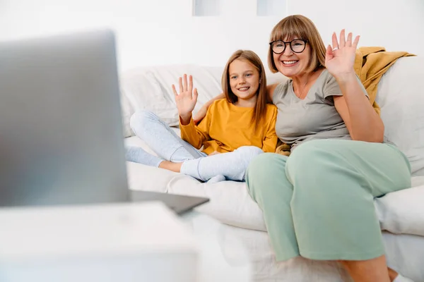 在家里沙发上使用笔记本电脑时 白人女孩和她的祖母正在打手势 — 图库照片