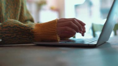 Kafede dizüstü bilgisayarda yazan sarı kazaklı bir kadın.