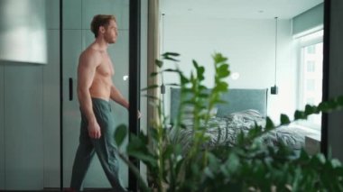 Ciddi sarışın atletik adam çıplak gövdesiyle eve yürüyor.