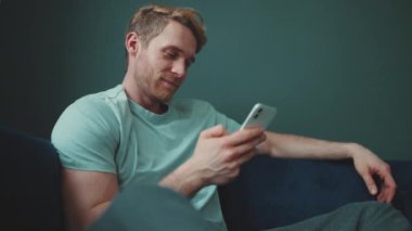 Meditative blond athletic man texting on mobile while sitting at home