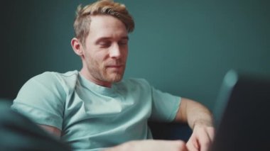 Evdeki kanepede otururken dizüstü bilgisayarda çalışan güzel sarışın atletik adam.