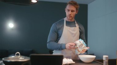 Serious blond athletic man pours frozen vegetables into a plate in the kitchen at home