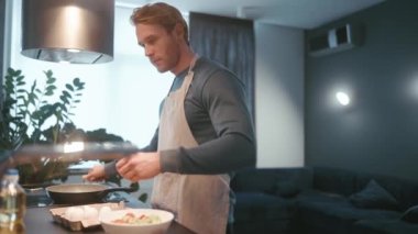 Concentrated blond athletic man pours oil into a frying pan in the kitchen at home
