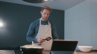 Concentrated athletic man mixing frozen vegetables on a frying pan in the kitchen at home