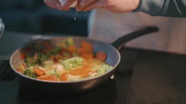 Male hands pours eggs to the vegetables in the pan in the kitchen