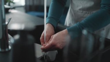 Önlük giyen atletik adam evdeki mutfakta bulaşıkları yıkıyor.