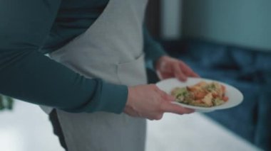 Concentrated man takes a plate of omelet with vegetables from the table and takes it away at home