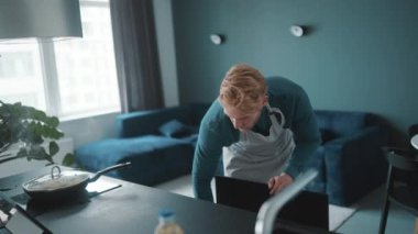 Confident athletic man wearing apron pours eggs with vegetables into plate in the kitchen