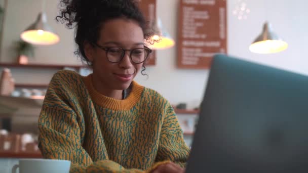 在咖啡店 穿着黄色毛衣和眼镜在笔记本电脑上工作的积极女性 — 图库视频影像
