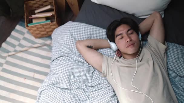 Hezký Asijský Muž Poslech Hudby Sluchátkách Zavřenýma Očima Zatímco Ležel — Stock video