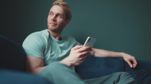 Positive Blond Athletic Man Texting Mobile Looking Side While Sitting — Vídeo de Stock