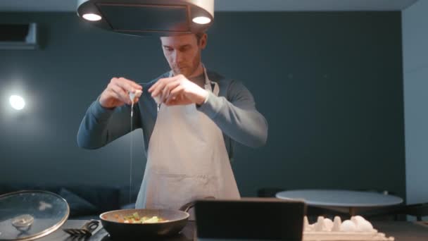 Blond Athletic Man Wearing Apron Pours Eggs Vegetables Pan Kitchen — Stockvideo