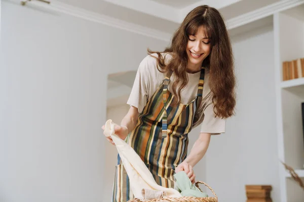 White young woman in apron smiling while doing housework at home