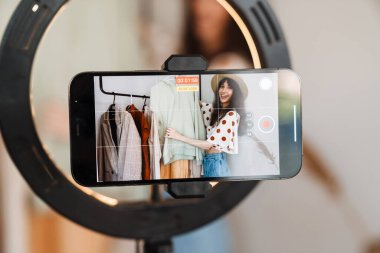 Beyaz kadın evde cep telefonundan selfie çekerken kıyafetlerini gösteriyor.
