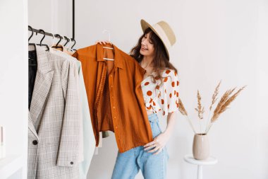 Beyaz kadın şapkalı, gülümseyen ve kıyafetlerini gardıropta tutan.