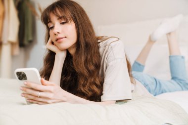 Beyaz kadın evde yatarken cep telefonu kullanıyor.