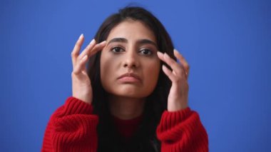 Yakışıklı Hintli esmer kadın mavi arka planda izole edilmiş kameraya bakışını düzeltiyor.