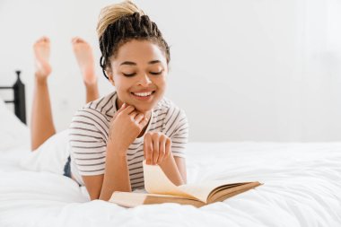 Genç siyahi kadın evde yatarken kitap okuyor.