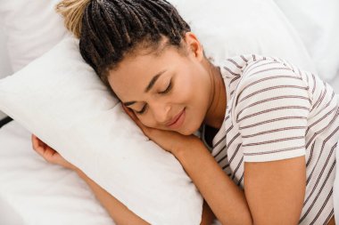 Young black woman with pigtails smiling while lying in bed at home