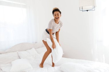 Genç siyahi kadın evde yastıkla eğlenirken gülüyor.