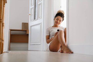 Genç siyahi kadın evde otururken cep telefonu kullanıyor.