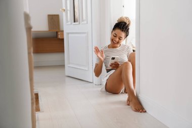 Genç siyahi kadın evde otururken cep telefonu kullanıyor.