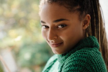 Evde çay içerken saçı örgülü genç siyah kadın gülümsüyor.