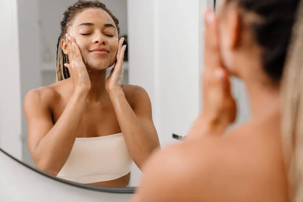 Young black woman cleaning her face with beauty product at bathroom