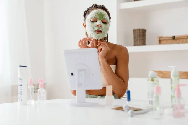 Young Black Woman Cosmetic Mask Looking Mirror Home — Fotografia de Stock