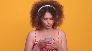 Pretty curly haired blonde woman listening music in headphones and dancing in the yellow studio
