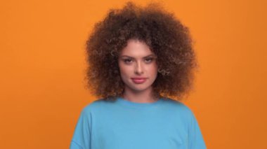 Laughing curly haired blonde woman wearing blue t-shirt opening eyes at the camera in the orange studio