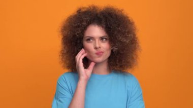 Positive curly haired blonde woman wearing blue t-shirt having an idea in the orange studio