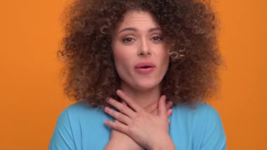Cute curly haired blonde woman wearing blue t-shirt looking at the camera in the orange studio
