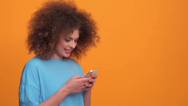 Позитивная Кудрявая Блондинка Синей Футболке Печатающая Мобильном Телефоне Оранжевой Студии — стоковое видео
