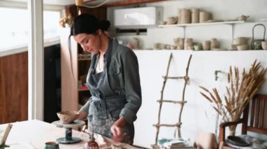 Neşeli kadın çömlekçi kil ürünün kenarlarını hizalar ve atölyedeki kameraya bakar.