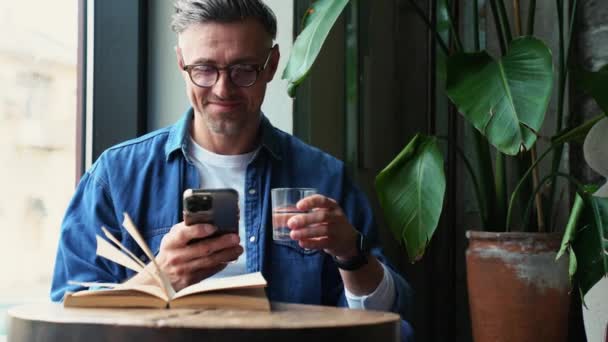 Happy Grey Haired Man Typing Phone Drinking Water While Sitting — ストック動画