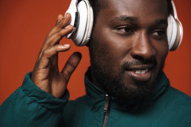 Kahverengi duvardan izole edilmiş kulaklıklarla müzik dinlerken gülümseyen siyah tüylü adam.