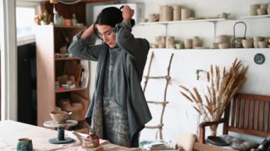 Güzel kadın çömlekçi önlük takıyor ve kilden ürünün kenarlarını içeride hizalıyor.