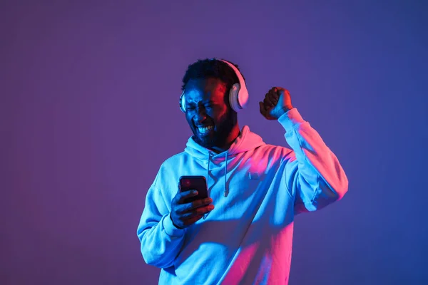Black man dancing and smiling while listening music isolated over purple wall