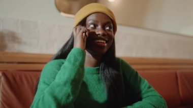 Sarı şapkalı gülümseyen Afrikalı genç kadın kafede telefonla konuşuyor.