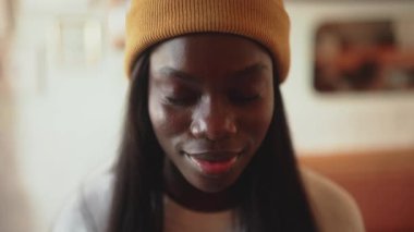 Laughing African young woman wearing white sweater opening eyes at the camera in cafe