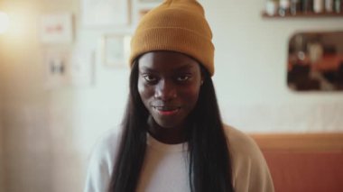 Smiling African young woman wearing white sweater opening eyes at the camera in cafe