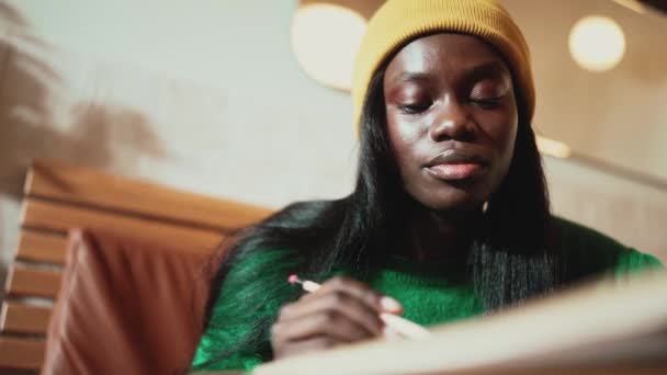 Concentrated African Young Woman Wearing Yellow Hat Writing Something Notepad — Videoclip de stoc