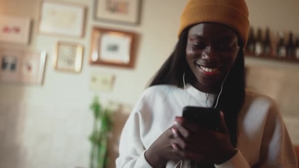 Nevető Afrikai Fiatal Fehér Pulóvert Visel Sms Mobilon Fülhallgatóban Kávézóban — Stock videók