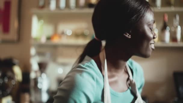 Улыбающаяся Африканка Бариста Белом Фартуке Ставит Очки Полку Кафе — стоковое видео