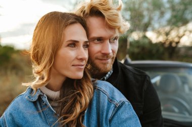 Yolculuk sırasında arabada beklerken gülümseyen ve sarılan beyaz bir çift.